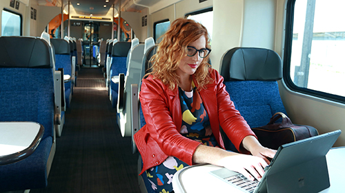 Image of a lady working on her laptop while sitting down at a table on a train